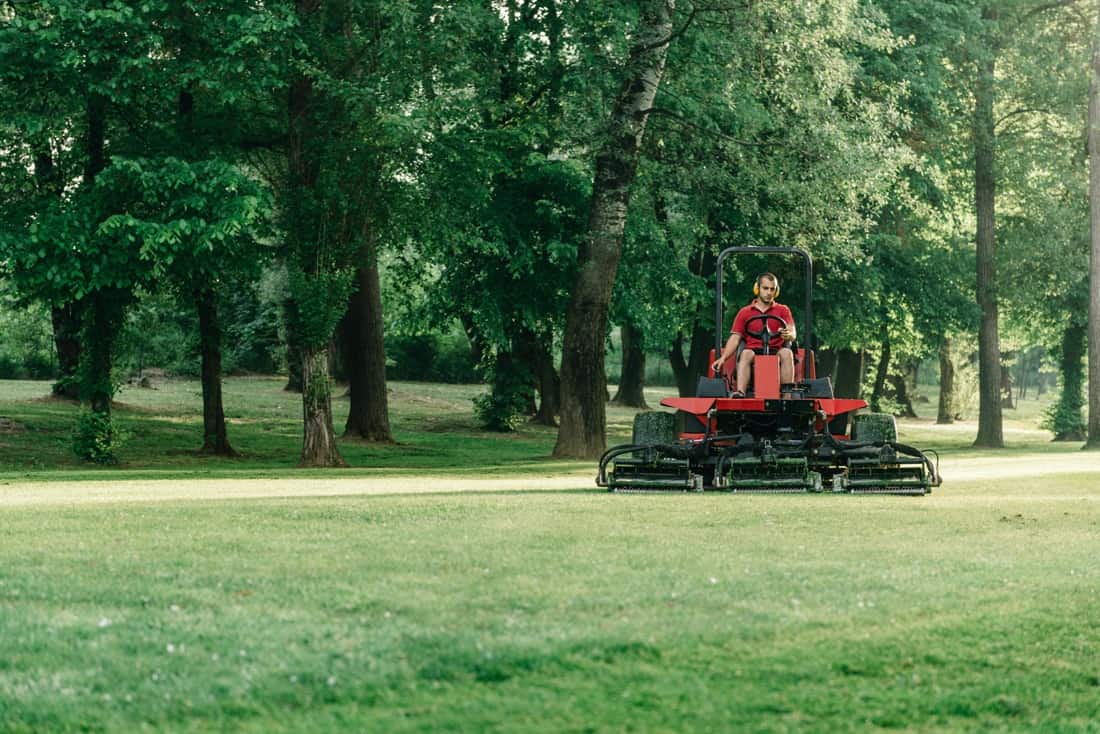 Modern mowing equipment trimming a lush green lawn with trees behind